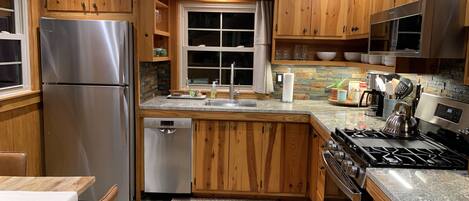 Una cocina con armarios de madera, electrodomésticos de acero inoxidable, salpicadero de piedra y una ventana con cortinas.