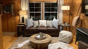 A cozy room with a wooden interior, featuring a leather sofa, a round wooden coffee table, a fireplace, and a television.