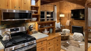 A kitchen with wooden cabinets, a stainless steel microwave, a stove, and a flat-screen TV.