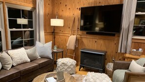 A cozy living room with a brown leather sofa, a round wooden coffee table, and a fireplace.