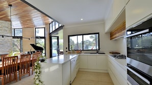A modern kitchen with white cabinetry, a large window, and a dining area with wooden chairs. - Stunning home on 5 acres with Infinity Pool & Fireplace (Herron)