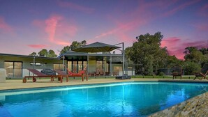 A modern pool area with clear blue water, a glass-enclosed structure, and outdoor seating. - Stunning home on 5 acres with Infinity Pool & Fireplace (Herron)