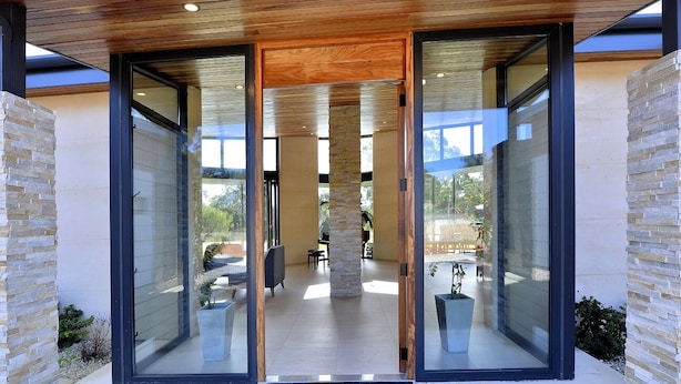 A modern entrance with glass doors, a stone pillar, and a view of the interior patio area. - Stunning home on 5 acres with Infinity Pool & Fireplace (Herron)