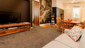 A modern living room with a flat-screen TV, wooden entertainment unit, and a dining area with a wooden table and chairs. - Court House Hideaway by Your Innkeeper Mudgee (Mudgee)
