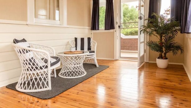 A room with a wooden floor, white wicker furniture, a potted plant, and a view through an open door. - Court House Hideaway by Your Innkeeper Mudgee (Mudgee)