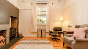 A cozy living room with a fireplace, a grey sofa, a black office chair, and a patterned rug. - Court House Hideaway by Your Innkeeper Mudgee (Mudgee)