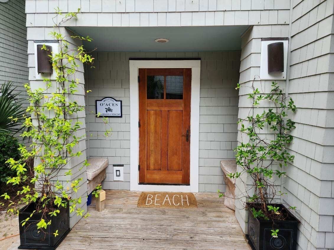 A house entrance with a wooden door, a welcome sign, and a 'BEACH' mat.