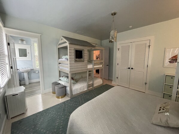 A bedroom with bunk beds, a large bed, a bathroom with a sink and mirror, and a closet with double doors.
