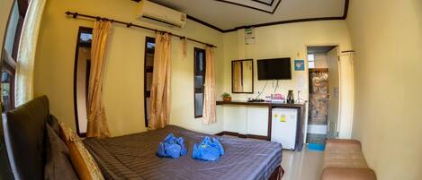 A hotel room with a bed, a desk, a TV, and a bathroom visible through an open door.