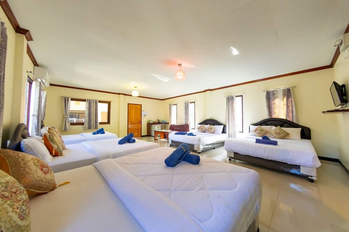 A hotel room with four beds, a desk, a chair, a TV, and a window.