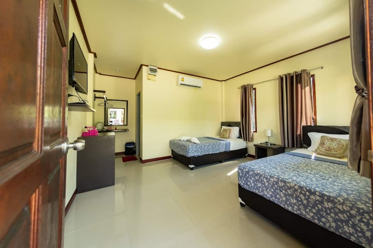 A hotel room with two beds, a desk, a television, and an air conditioning unit.