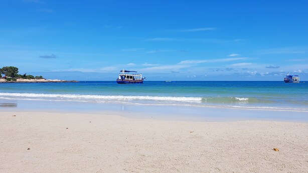 Ein Strand mit zwei Booten im Wasser und einem sandigen Ufer.