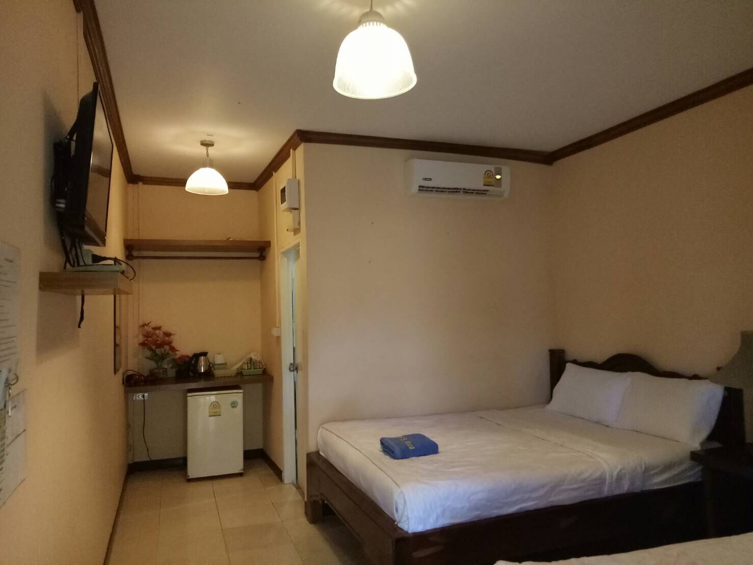 Une petite pièce, bien rangée, comprenant un lit, un bureau, un réfrigérateur et un téléviseur fixé au mur.