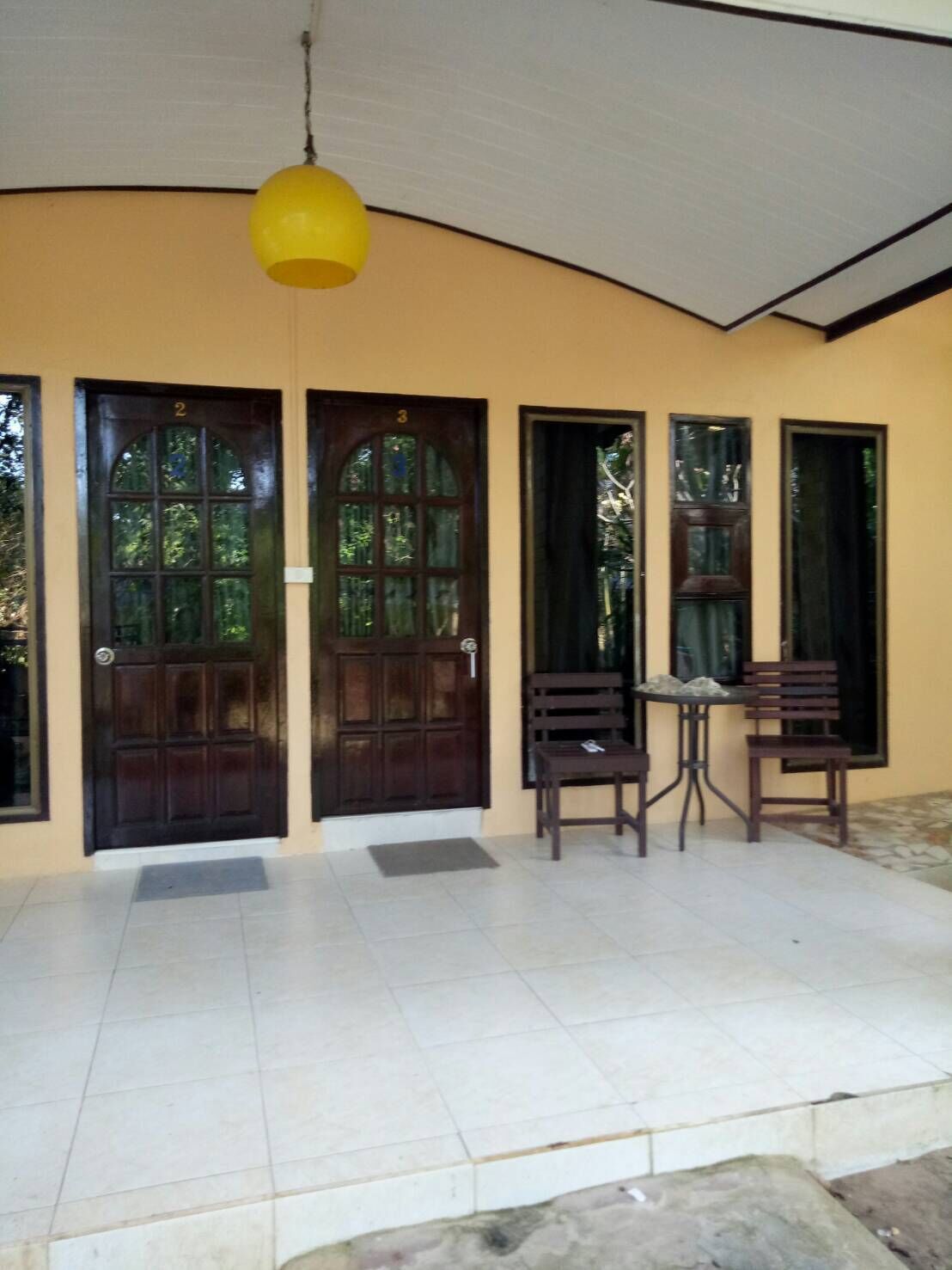 A covered outdoor area with a tiled floor, two wooden doors, and a yellow hanging light fixture.