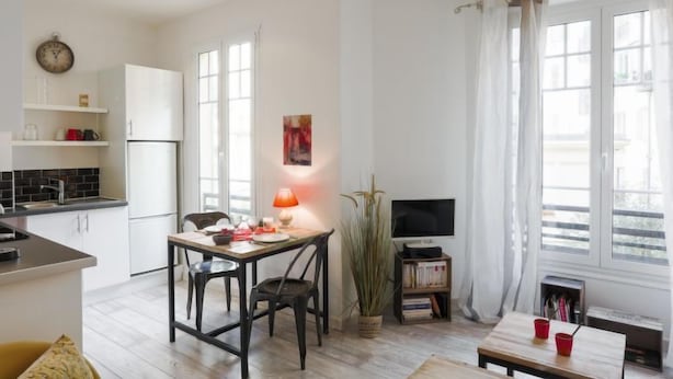 A modern apartment with a kitchen, dining area, and living room. It features a dining table with chairs, a TV, and a bookshelf.