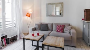 A modern living room with a sofa, two coffee tables, a floor lamp, a mirror, and a cabinet.