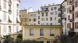 A multi-story residential building with balconies, a central entrance, and surrounding greenery.