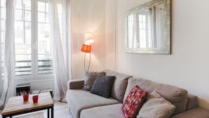 A cozy living room with a beige sofa, a wooden coffee table with red cups, a floor lamp, and a large mirror on the wall.