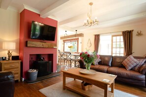 A living room with a fireplace, a television mounted on the wall, a sofa, and a dining area with a table and chairs.