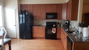 A kitchen with wooden cabinets, a black refrigerator, a microwave, and a stove. - Spacious Yet Cozy Edgewater Park Townhouse (Minutes to the Boardwalk) (Rehoboth Beach)