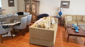A living room with a round dining table, grey upholstered chairs, a patterned sofa, a wooden cabinet, and a blue lamp. - Spacious Yet Cozy Edgewater Park Townhouse (Minutes to the Boardwalk) (Rehoboth Beach)