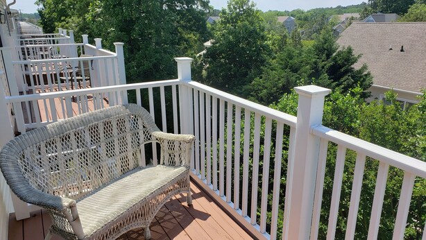 A balcony with wicker furniture, white railings, and a view of a residential area. - Spacious Yet Cozy Edgewater Park Townhouse (Minutes to the Boardwalk) (Rehoboth Beach)
