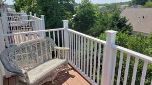 Un balcon doté de meubles en osier, de balustrades blanches et offrant une vue sur un quartier résidentiel.