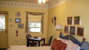 Una habitación de hotel con cama, escritorio, silla, lámpara y cuadros en la pared.