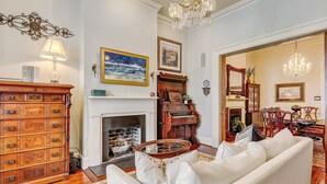 A spacious living room with a fireplace, a piano, and a chandelier. - Exquisite Estate on Broughton Street! (Savannah)