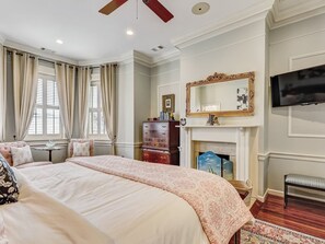 A spacious bedroom with a large bed, a fireplace, a television, and a window with curtains. - Stunning Historic Home on Broughton St (Savannah)
