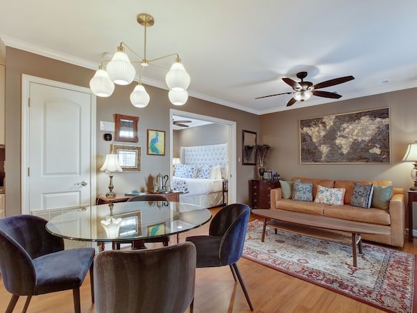 Relax in this stylish living room with a glass-top dining table, comfortable sofa, and a beautiful abstract painting.