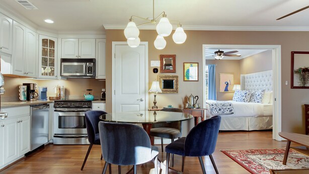 A modern kitchen with white cabinets, a dining table with chairs, and a bedroom with a bed and a ceiling fan. - Lovely Carriage House In the Middle of Downtown! (Savannah)
