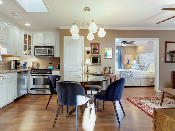 Una cocina moderna con armarios blancos, una mesa de comedor con sillas, y un dormitorio con cama y ventilador de techo.