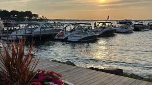 Un puerto deportivo con barcos amarrados, una terraza de madera y un atardecer al fondo.