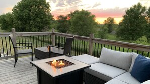Una terraza con un hogar para fuego, mobiliario exterior y vista al atardecer.