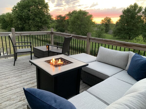 Eine Terrasse mit Feuerstelle, Gartenmöbeln und Blick auf den Sonnenuntergang.