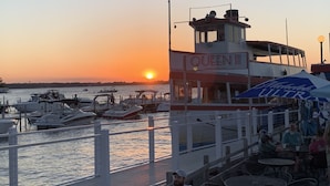Un restaurante frente al agua llamado 'Queen III' con terraza y vistas al atardecer sobre el agua.