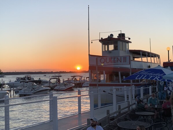 A waterfront restaurant named 'Queen III' with outdoor seating and a view of the sunset over the water.