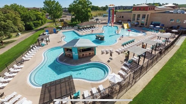 Una gran piscina al aire libre con varias secciones y un tobogán acuático, rodeada de tumbonas y sombrillas.