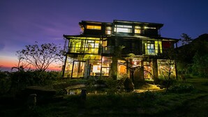 Una casa a più piani con ampie finestre e un balcone, immersa nel verde.