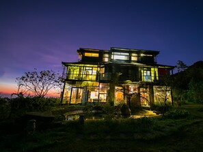 Ein mehrstöckiges Haus mit großen Fenstern und einem Balkon, umgeben von viel Grün.