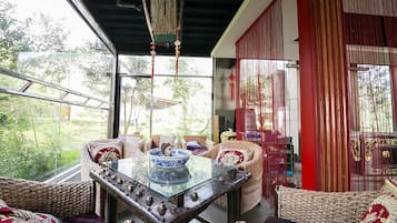 A room with a glass table, wicker furniture, and a view of greenery outside.
