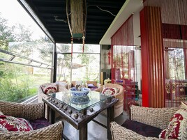 A room with a glass table, wicker furniture, and a view of greenery outside.