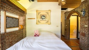 A hotel room with a bed, a teddy bear, a framed picture, and brick walls.