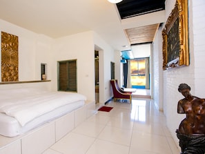 Ein Hotelzimmer mit einem großen Bett, einem Sessel, einer Statue und Blick auf den Sonnenuntergang durch das Fenster.