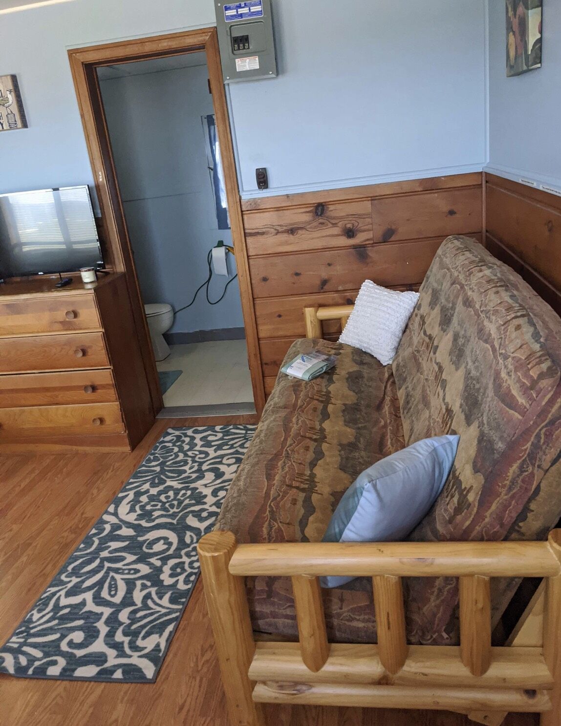 A wooden sofa with patterned cushions, a wooden dresser, and a patterned rug in a room with light blue walls.