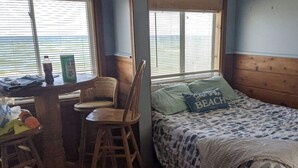 A small room with a bed, a table with chairs, and a view of the ocean through the window. -  #5-The Lazy Fish (Au Sable Charter Township)