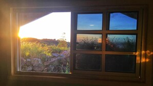 A window with a view of a sunset over a rocky landscape with grass and flowers. - OYO 90195 Anjung Rehat Jamsari (Ranau)