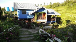 A blue house with a porch, surrounded by a garden with stepping stones leading to the entrance. - OYO 90195 Anjung Rehat Jamsari (Ranau)