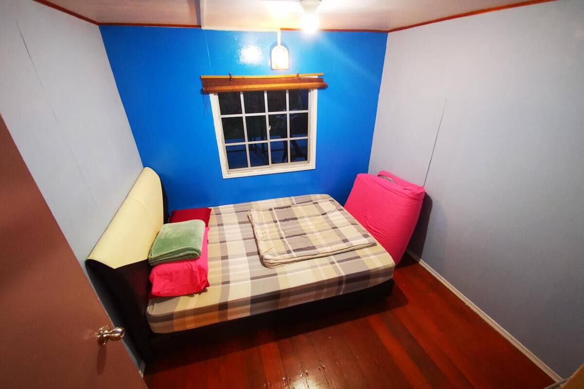 Una habitación pequeña con una cama, una ventana con persiana de madera y una lámpara de noche.